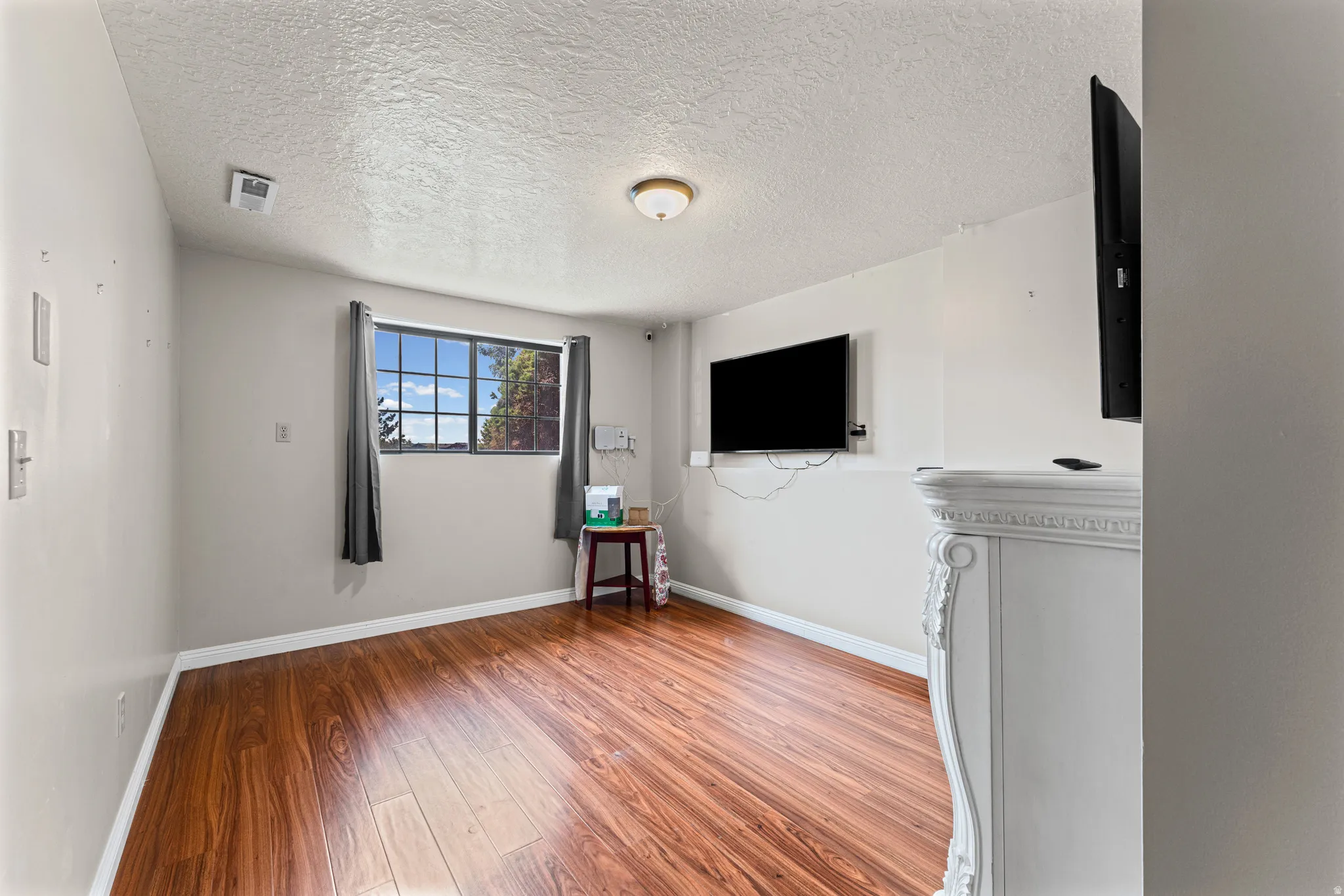 Interior space featuring wood-finish flooring, a window with exterior views, and a decorative white mantelpiece