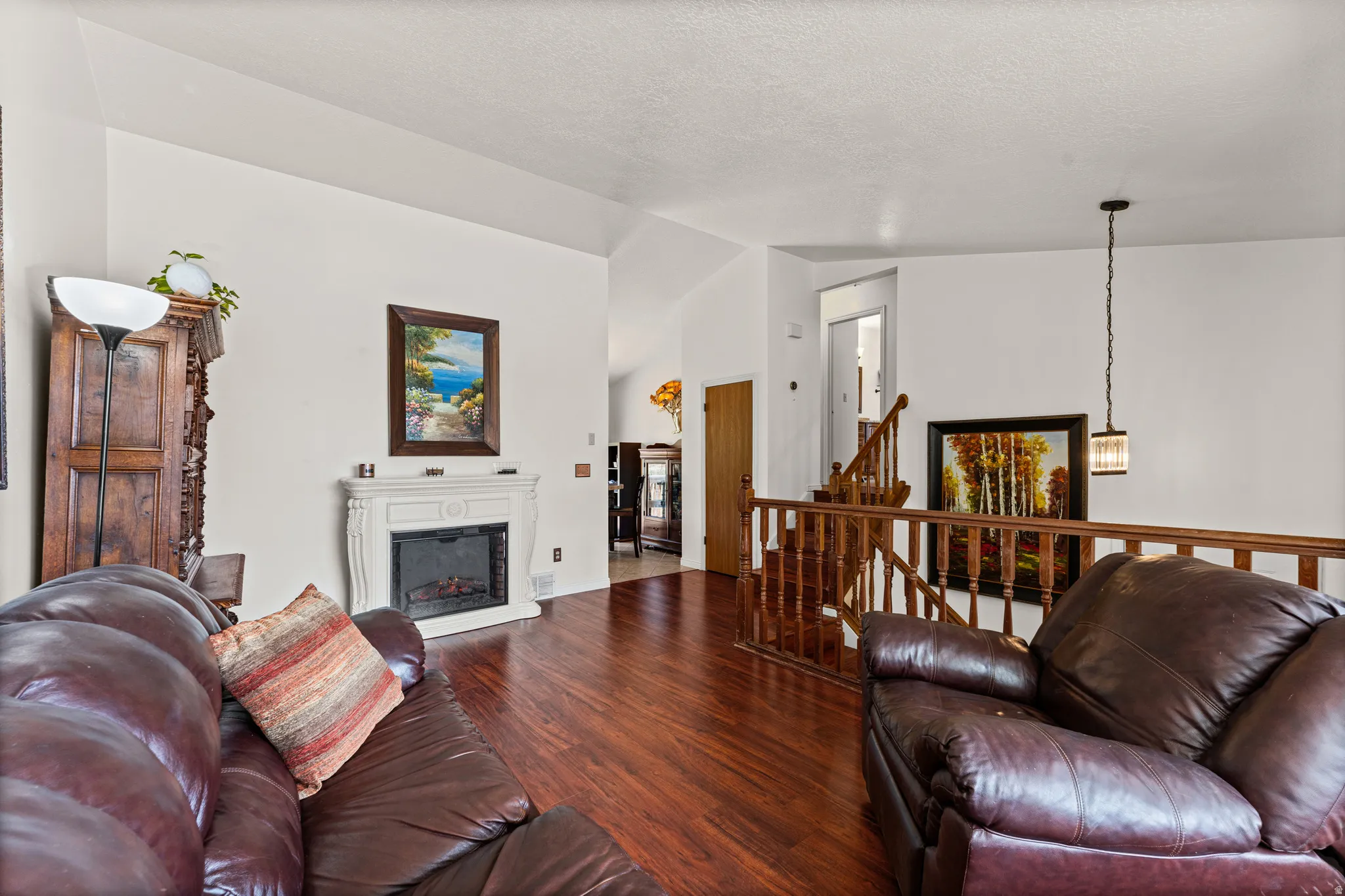 Living area featuring wood-finish flooring, a white mantel fireplace, and a wood railing staircase