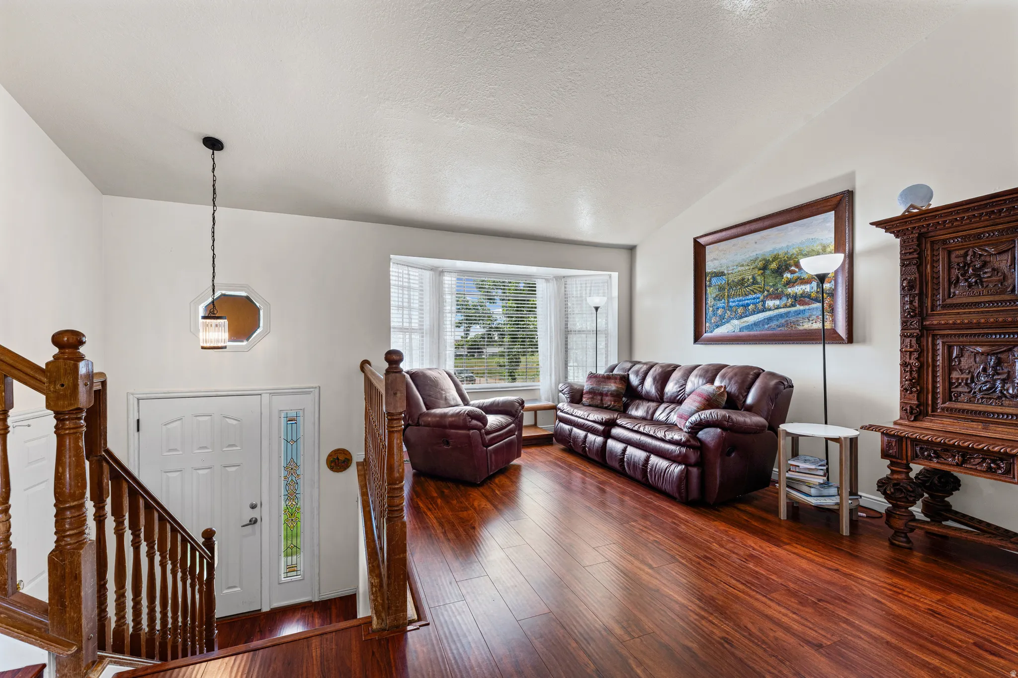 Entryway and living area featuring wood-finish flooring, a white paneled entry door with a decorative glass sidelight, and a prominent bay window