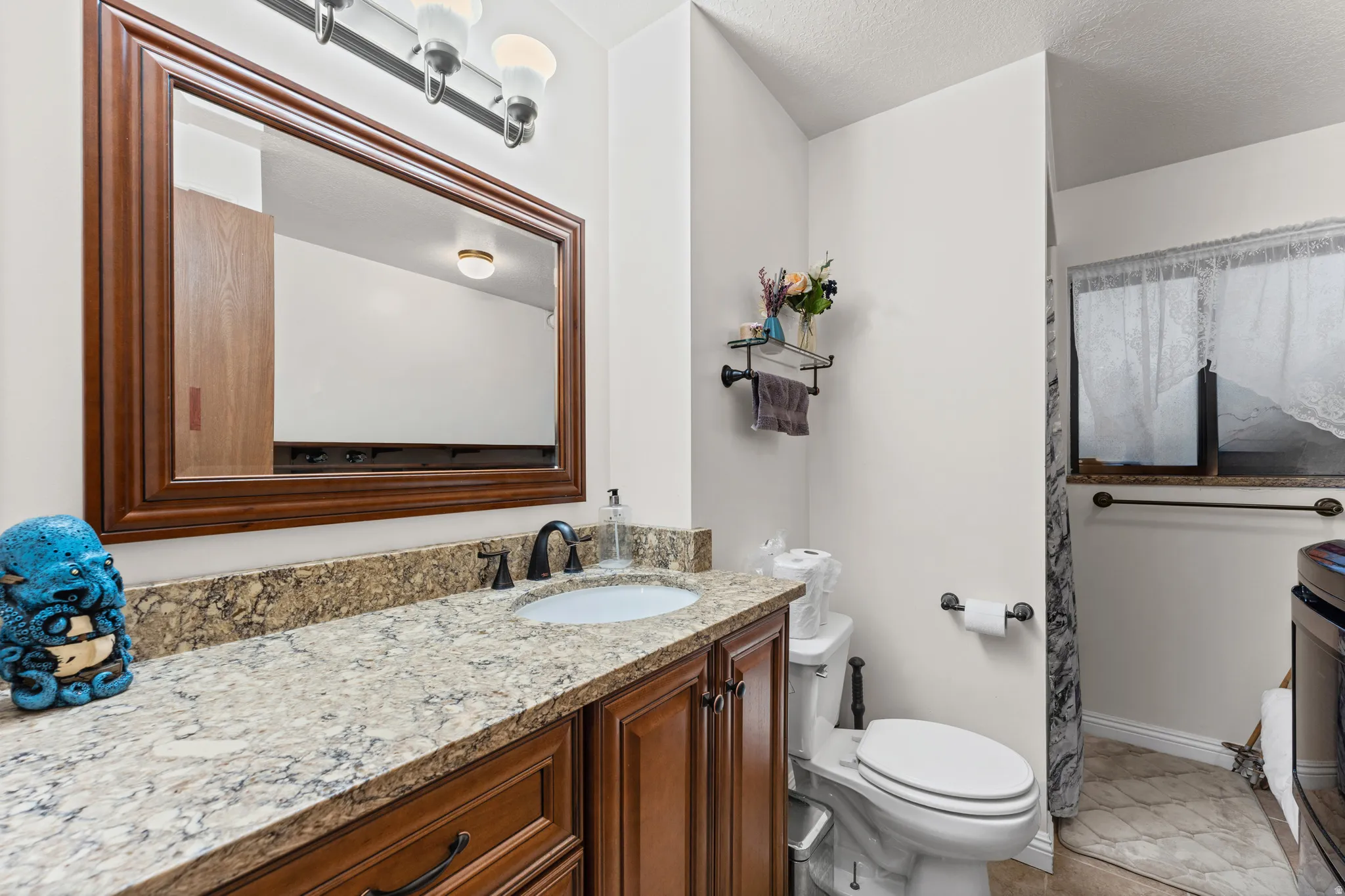 Bathroom featuring a wood-finish vanity with panel detailing, a light-toned patterned countertop, an undermount sink with a matte black faucet, and a large framed mirror with overhead vanity lighting