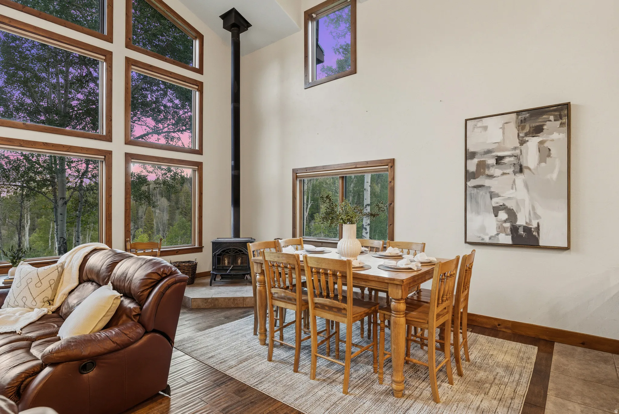 Expansive wood-framed windows, a corner wood-burning stove with a stone hearth, and a high vaulted ceiling define this interior space