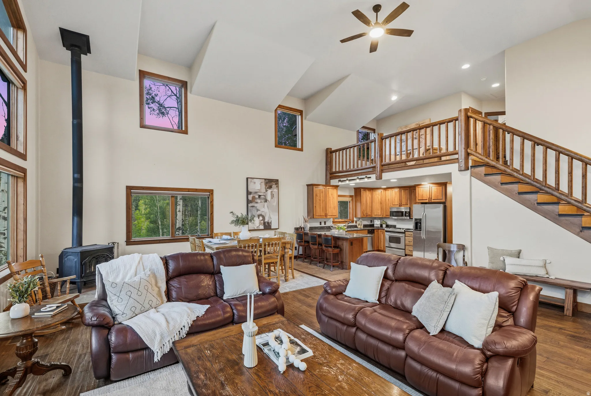 Vaulted living space featuring a wood-burning stove, rich wood-finish flooring, and multiple windows