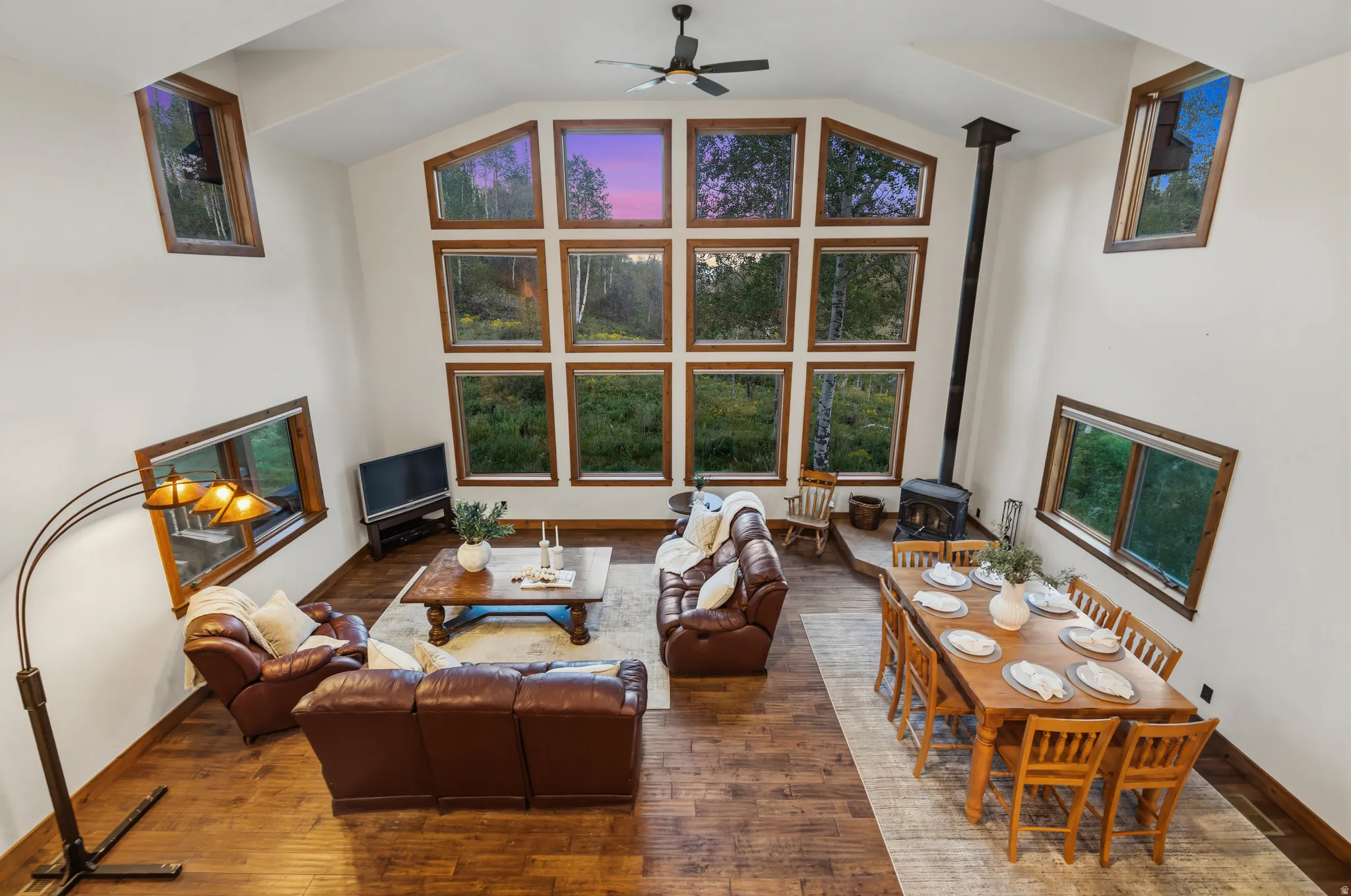 Vaulted ceiling living area featuring wood-finish flooring, a wood-burning stove, and a wall of multi-pane windows