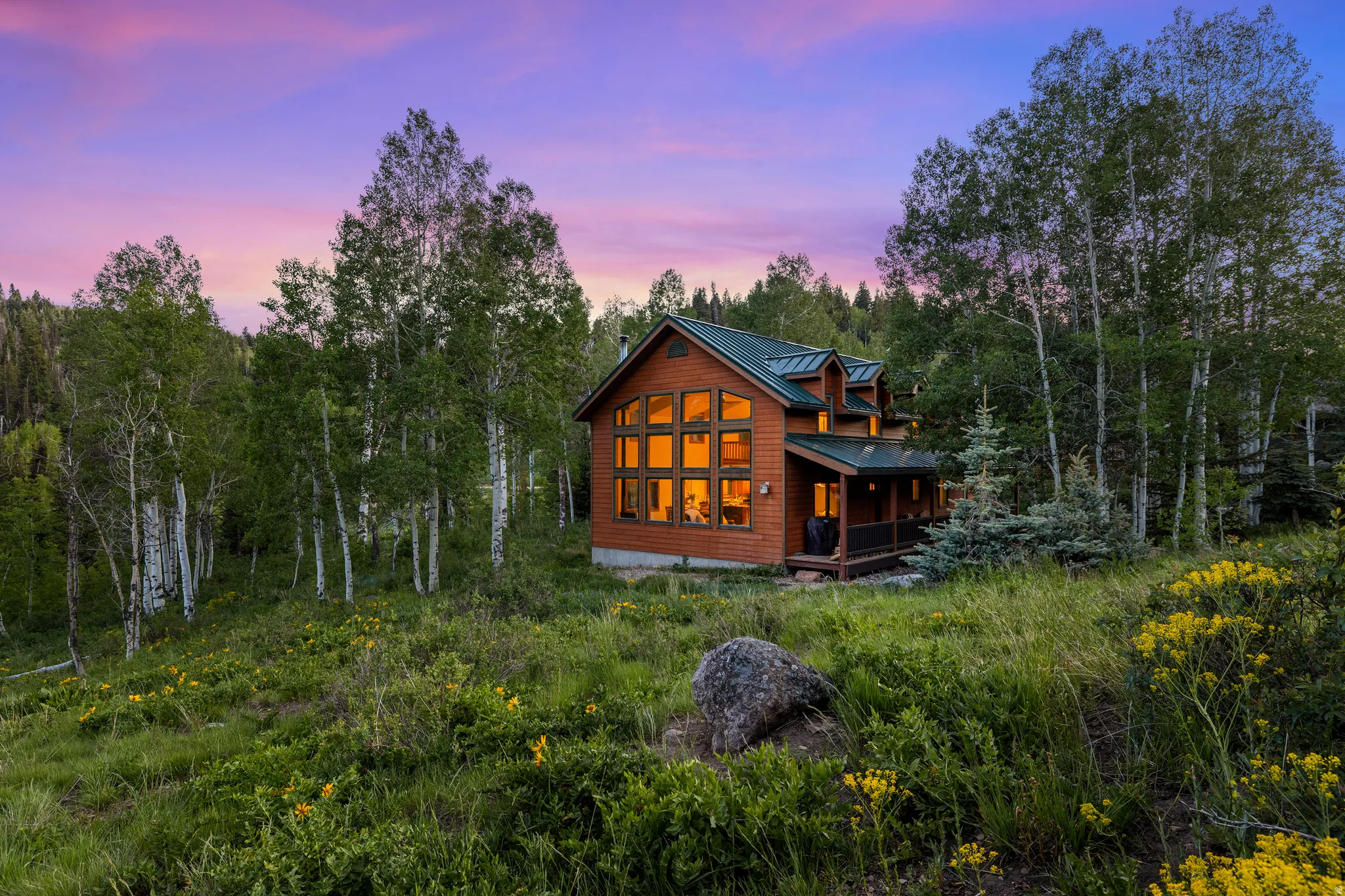 Log cabin exterior with a green metal roof, multiple dormer windows, and a covered porch