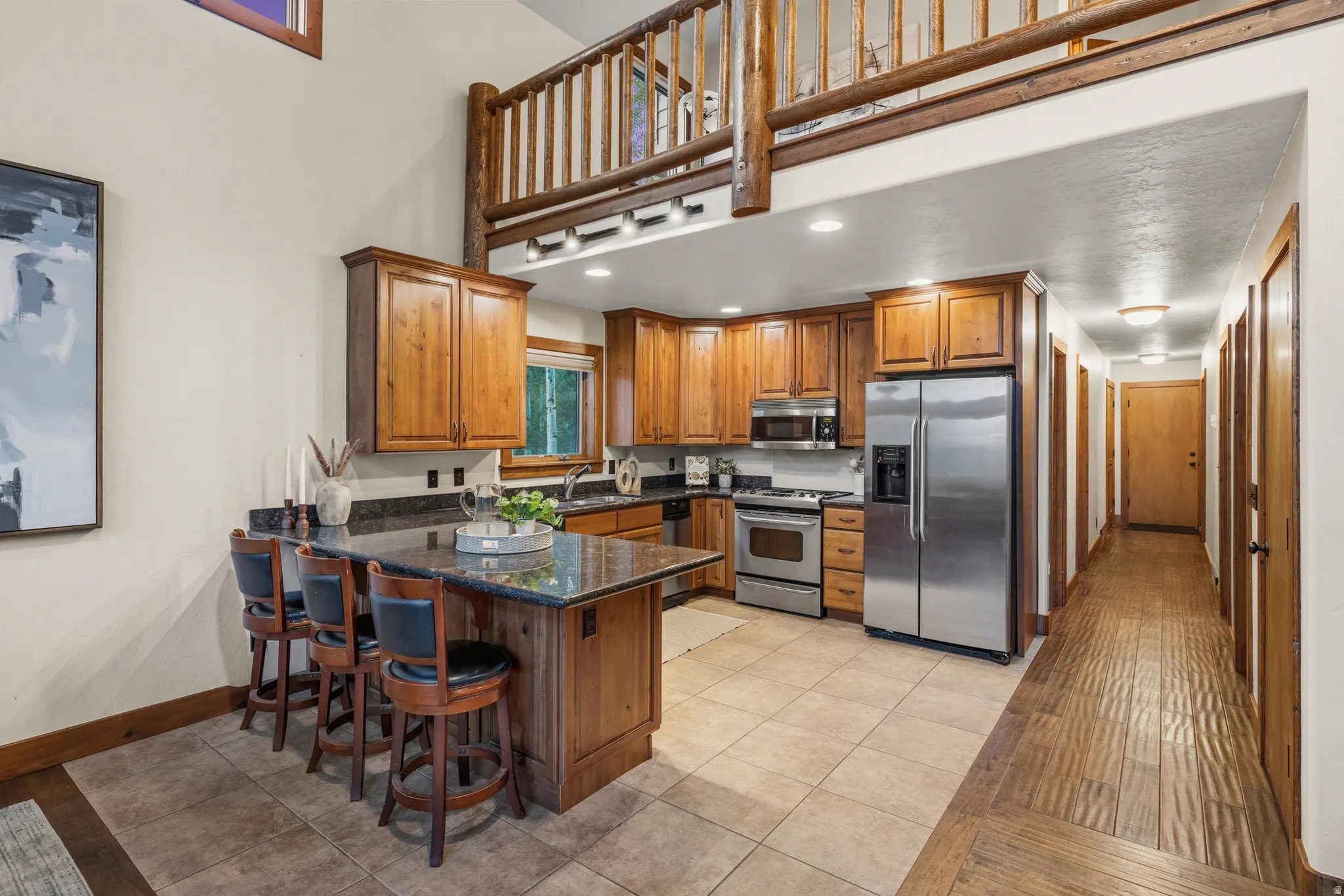 Kitchen featuring wood cabinetry, stainless steel appliances, dark countertops, and a breakfast bar with seating for three