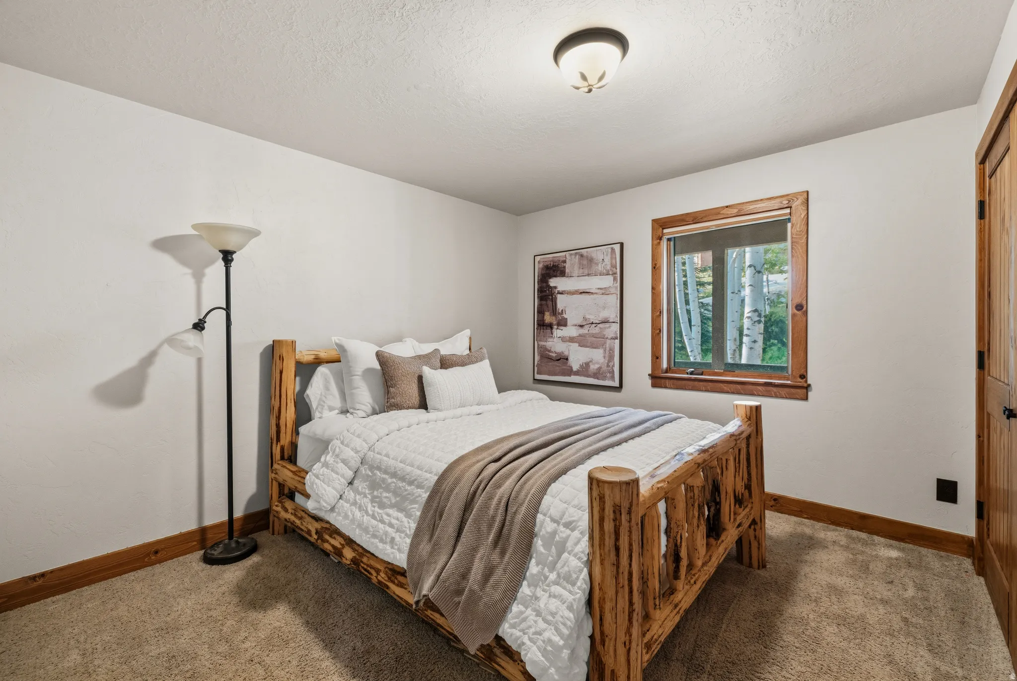Carpeted bedroom featuring a wooden window frame, a dark wood-finish door, and a flush mount ceiling light fixture