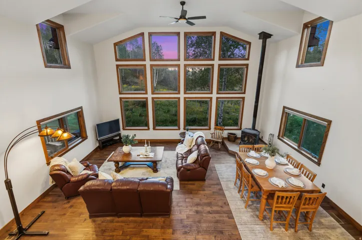 Vaulted ceiling living area featuring wood-finish flooring, a wood-burning stove, and a wall of multi-pane windows