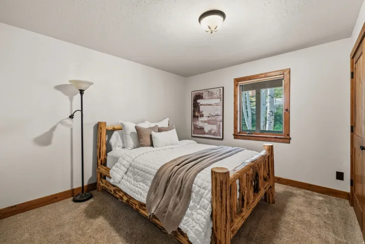 Carpeted bedroom featuring a wooden window frame, a dark wood-finish door, and a flush mount ceiling light fixture