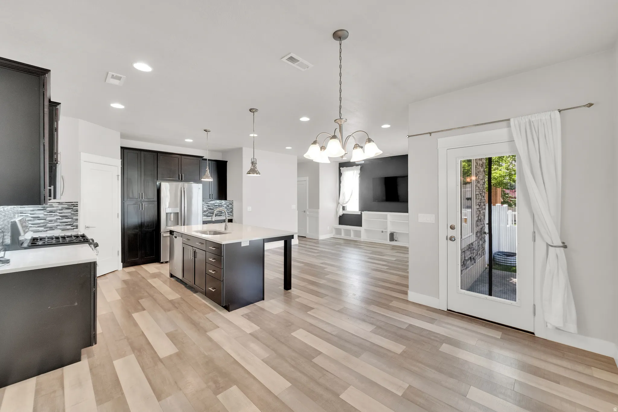 Open-concept living space featuring wood-finish flooring, a kitchen island with seating, dark wood cabinetry, stainless steel appliances, and a glass-paned exterior door