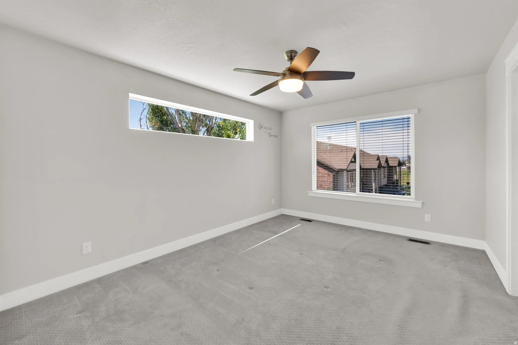 Spacious room featuring light gray walls, plush gray carpeting, and white baseboards