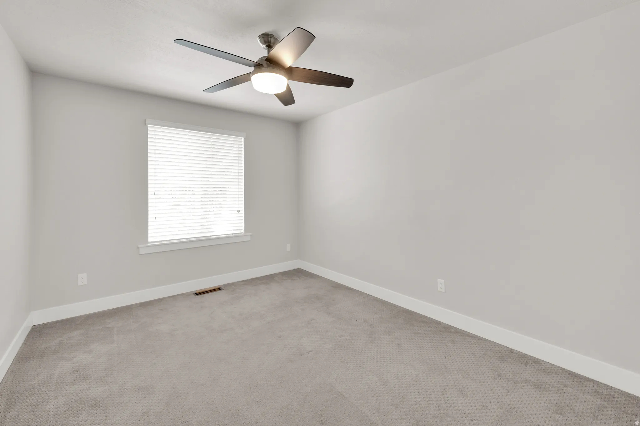 Neutral wall paint, ceiling fan with integrated lighting, window with blinds, baseboard trim, and gray carpeted flooring