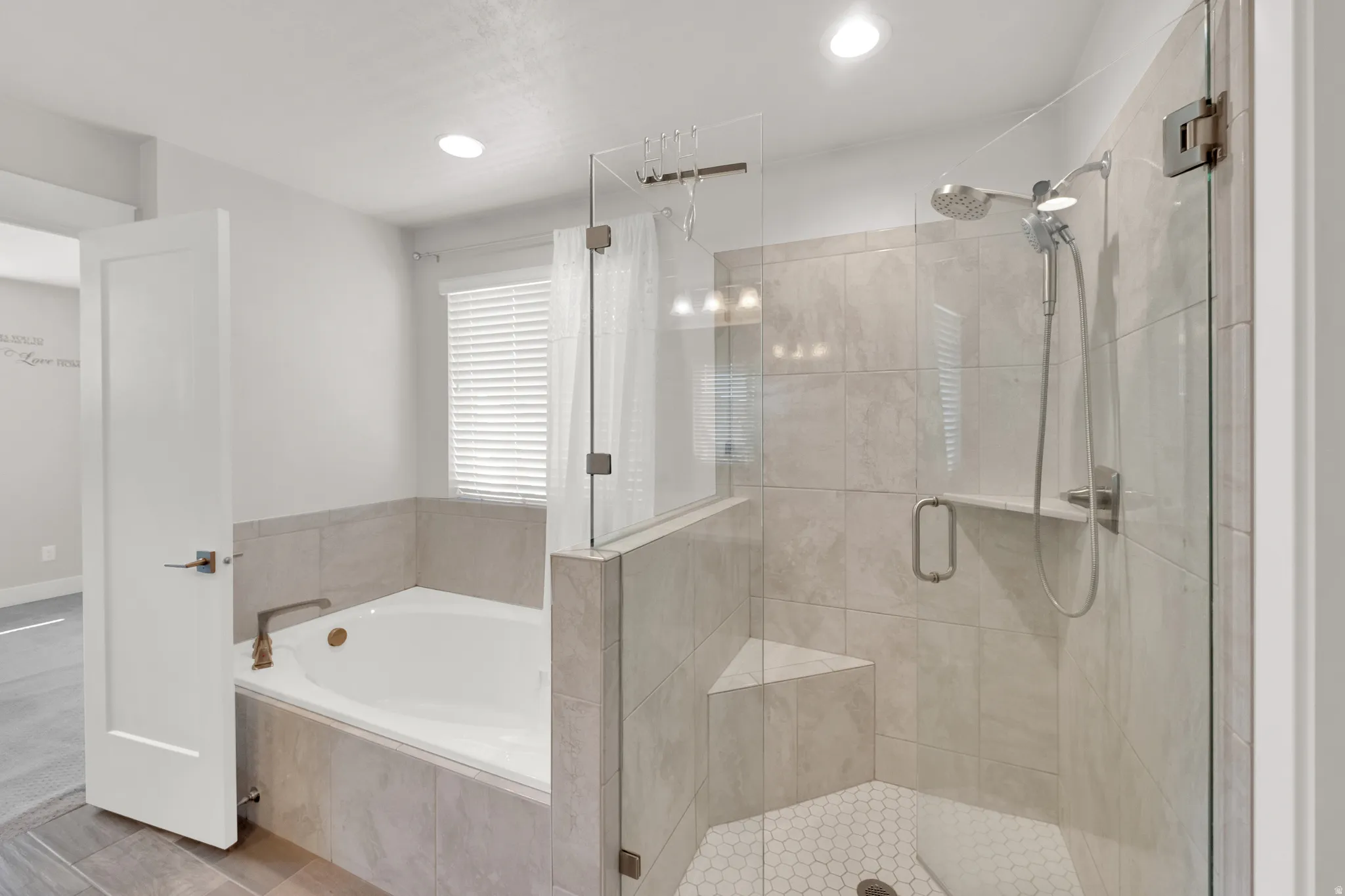 Spacious bathroom featuring a built-in soaking tub with a tiled surround, a separate glass-enclosed shower with a built-in bench, a handheld showerhead, and light-toned tile flooring