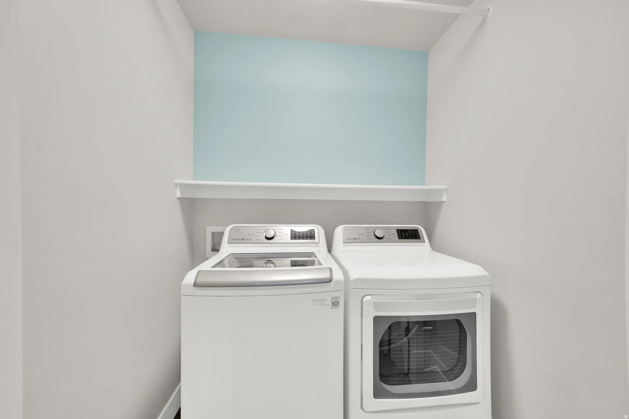 Dedicated laundry area featuring a white floating shelf, light blue accent wall, and integrated overhead shelving