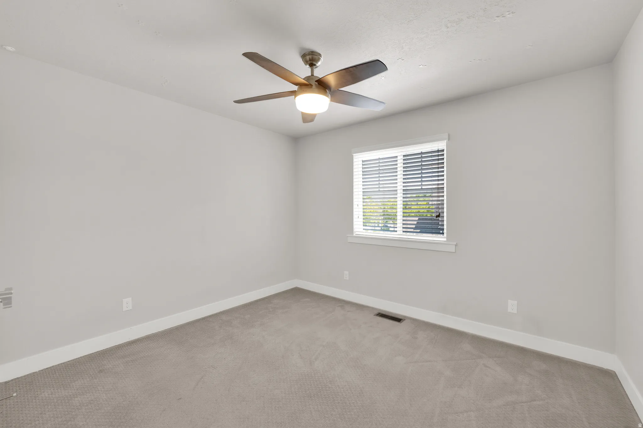 Neutral-toned room featuring a ceiling fan with integrated lighting, a window with horizontal blinds, gray textured carpeting, and white baseboards