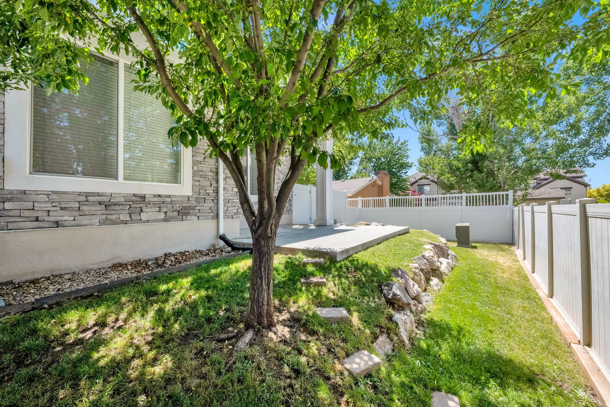 Rear exterior featuring stacked stone siding, white trim windows, and a concrete patio