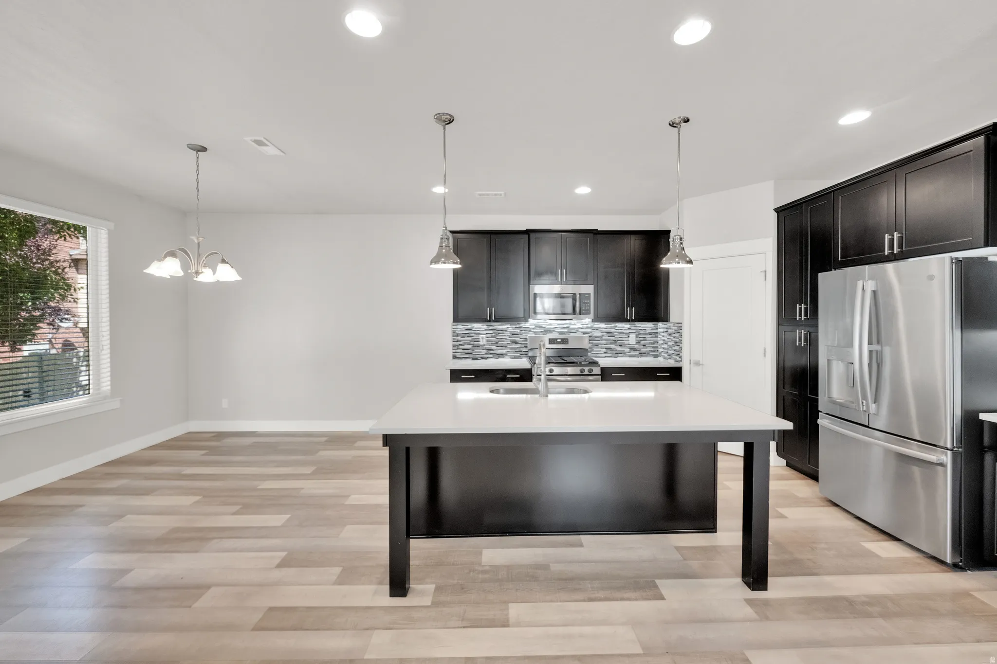 Modern kitchen featuring dark cabinetry, stainless steel appliances, a white island countertop, and light wood-finish flooring