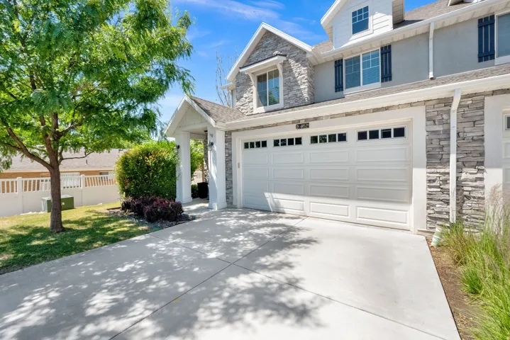 Stone and stucco exterior with a two-car garage, dormer window, and covered entryway