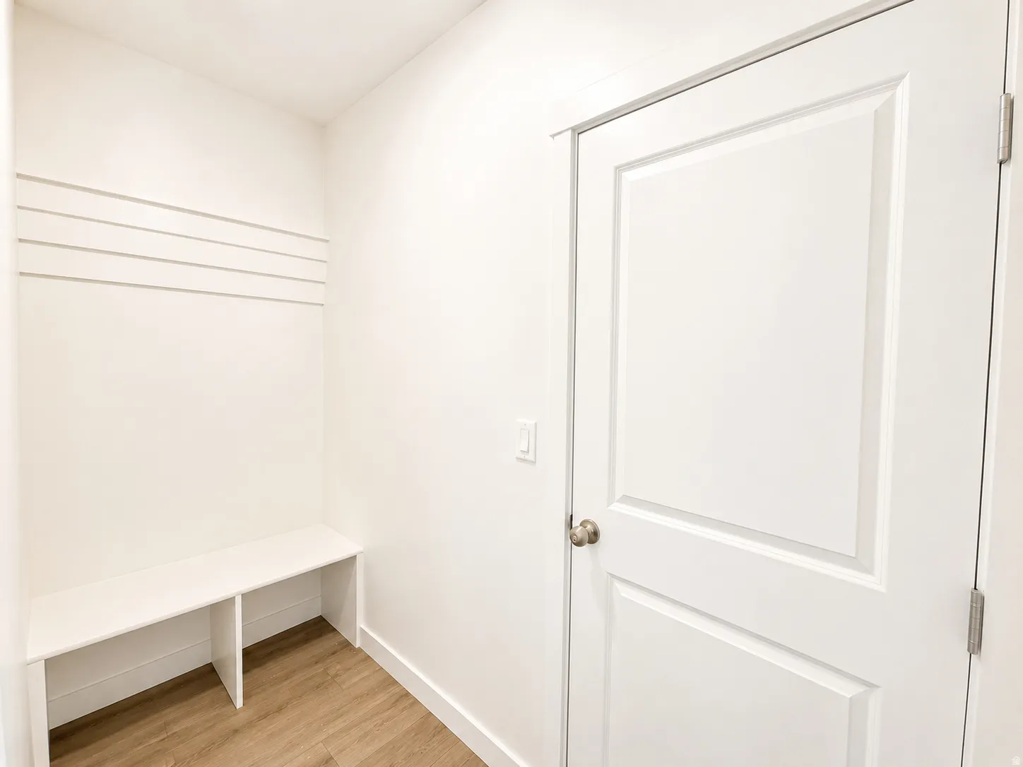Entryway featuring built-in bench seating, horizontal wall paneling, wood-finish flooring, and a paneled interior door with brushed nickel hardware