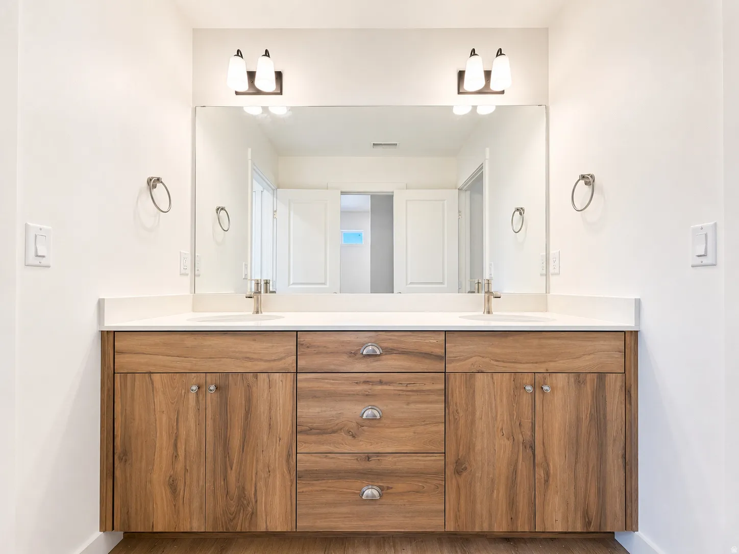 Double vanity featuring wood-finish cabinetry, white countertops, dual undermount sinks, and brushed nickel hardware