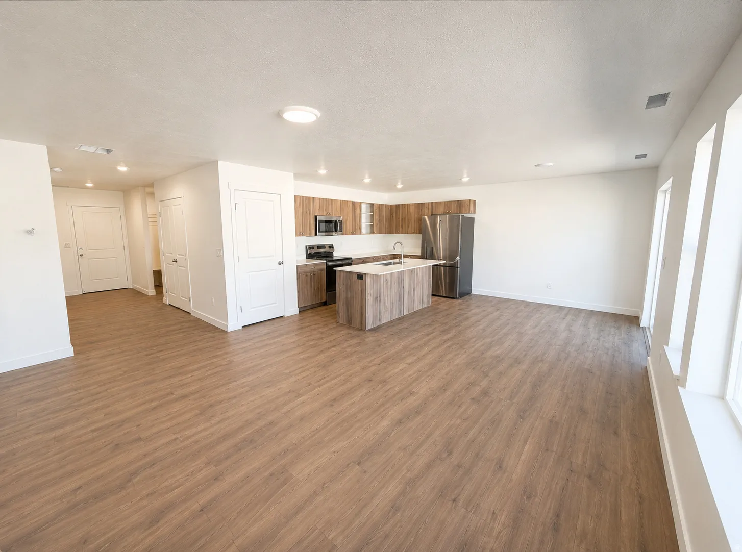 Open-concept living space featuring wood-finish flooring, a kitchen island with sink, stainless steel appliances, and multiple windows