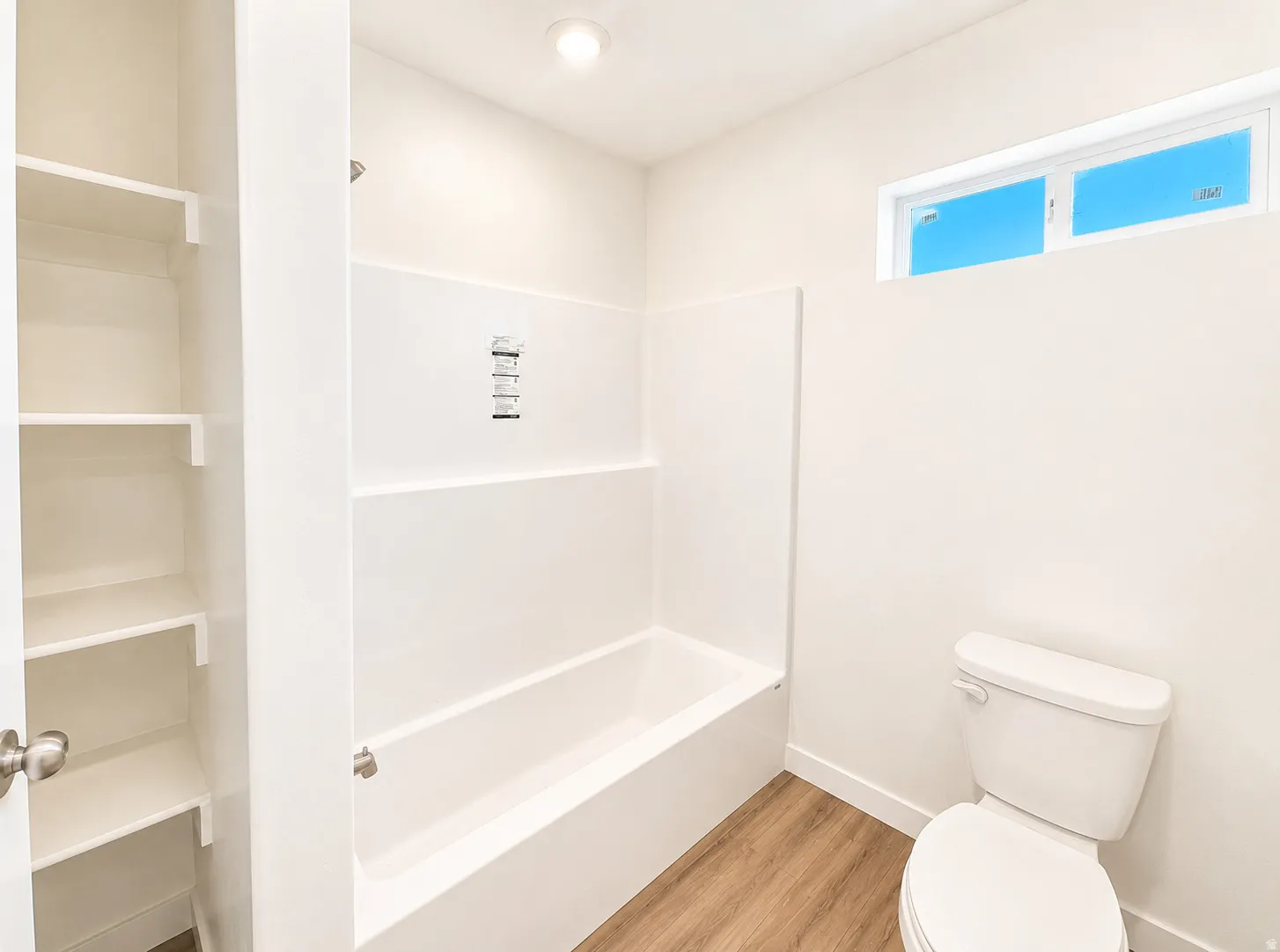Bathroom featuring a white tub-shower combination with chrome fixtures, a white toilet, and wood-finish flooring