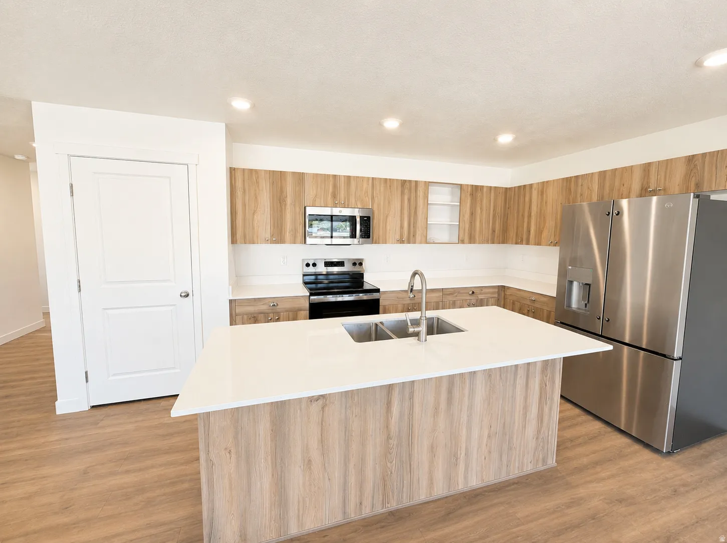 Kitchen featuring a center island with a double basin sink, white countertops, stainless steel appliances, wood-finish cabinetry, and wood-finish flooring