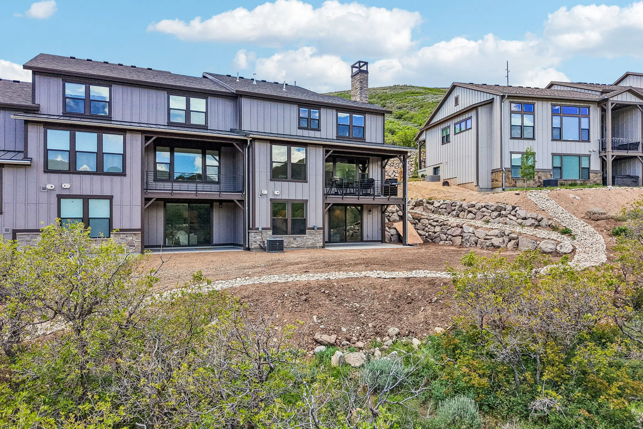 Contemporary multi-level exterior featuring vertical siding, stone accents, multiple large windows, and a covered balcony