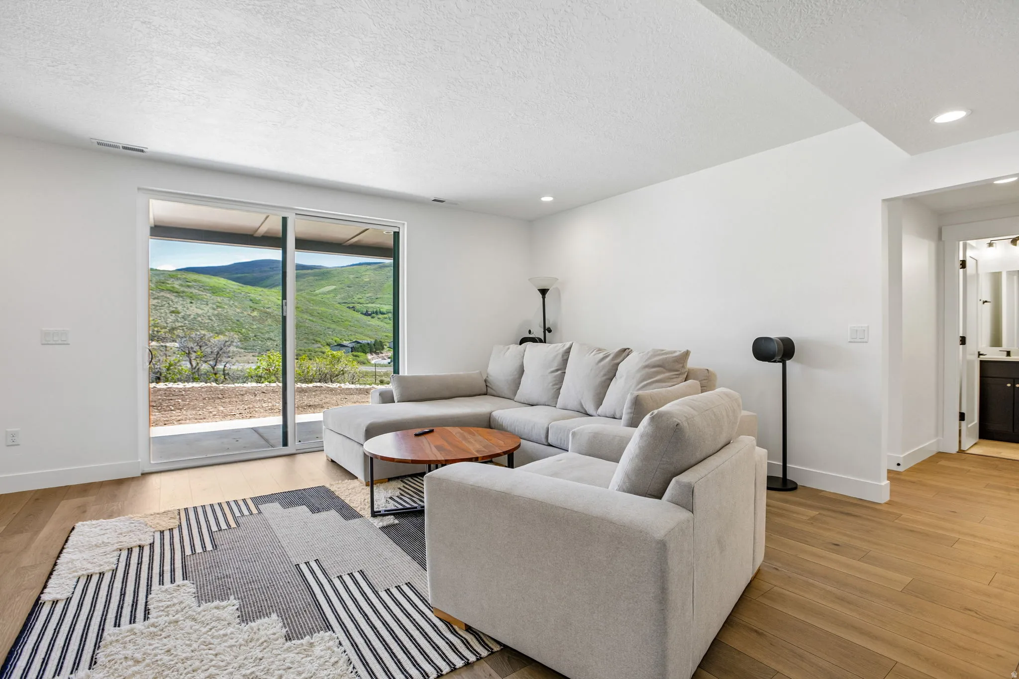 Sliding glass door opening to outdoor space, featuring light wood-finish flooring, recessed ceiling lighting, and white walls