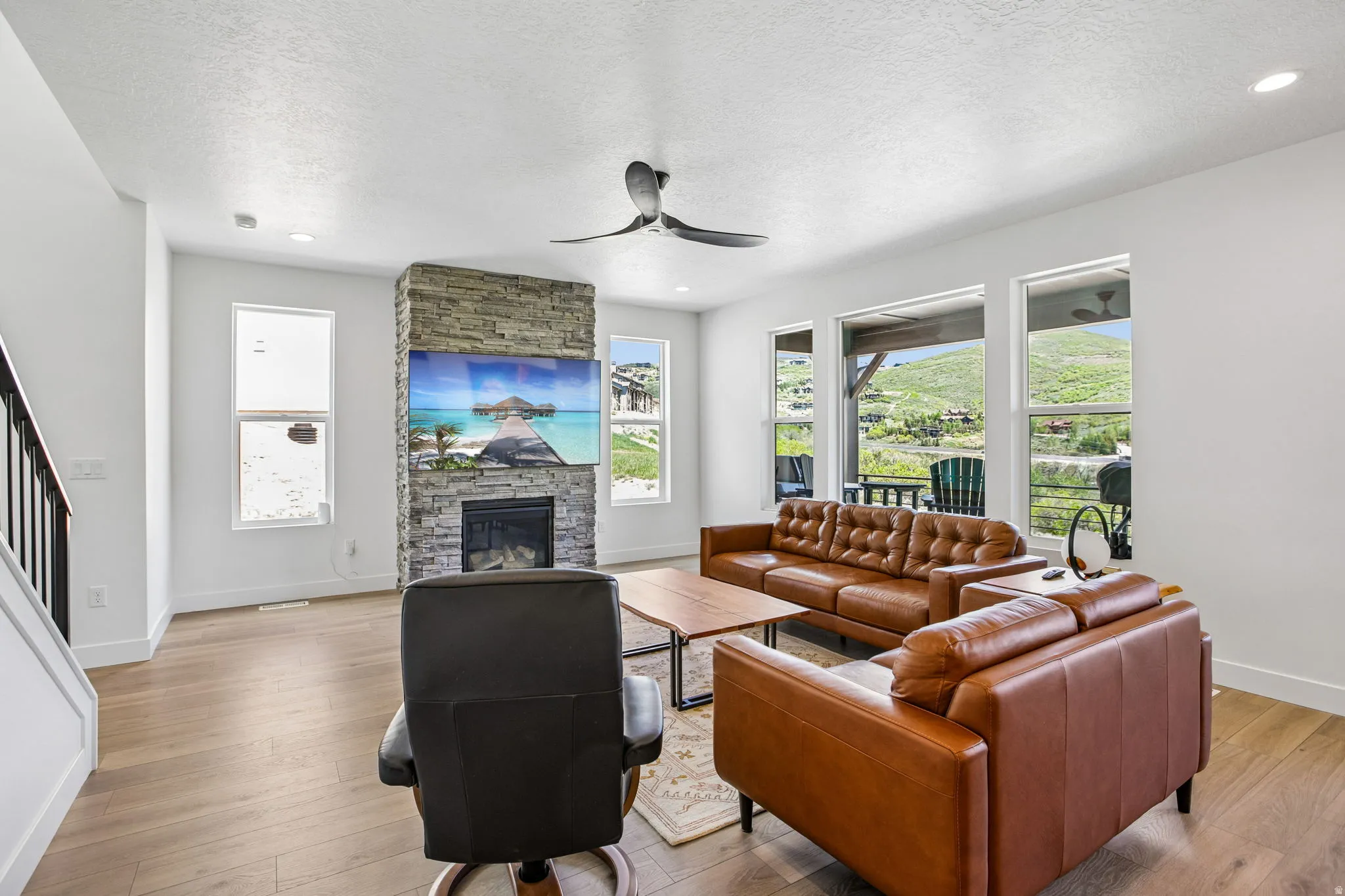 Living area featuring wood-finish flooring, a stacked stone fireplace with an integrated television, and a contemporary ceiling fan