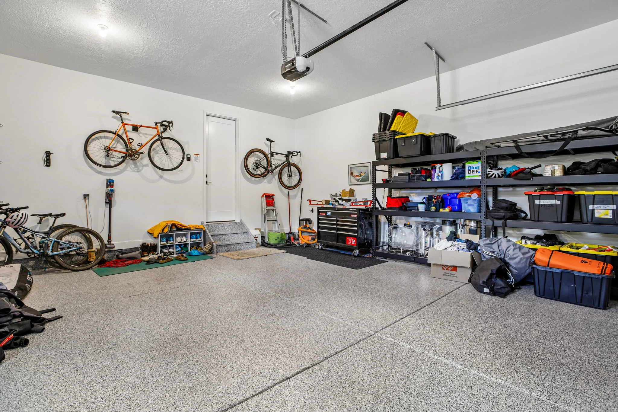 Spacious garage featuring a durable epoxy-coated floor, bright overhead lighting, a white pedestrian door, and built-in shelving for organized storage