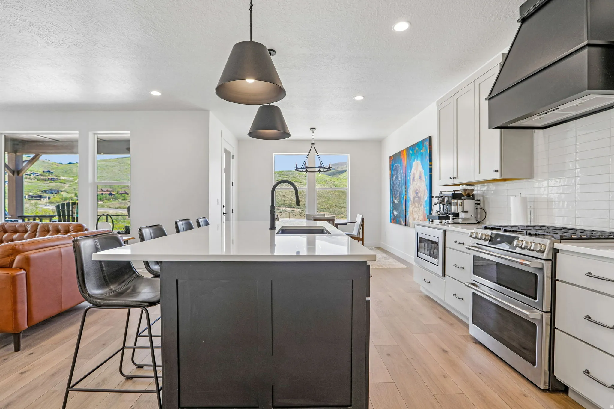 Open-concept kitchen featuring a large island with seating, stainless steel appliances, white cabinetry, wood-finish flooring, and a white subway tile backsplash
