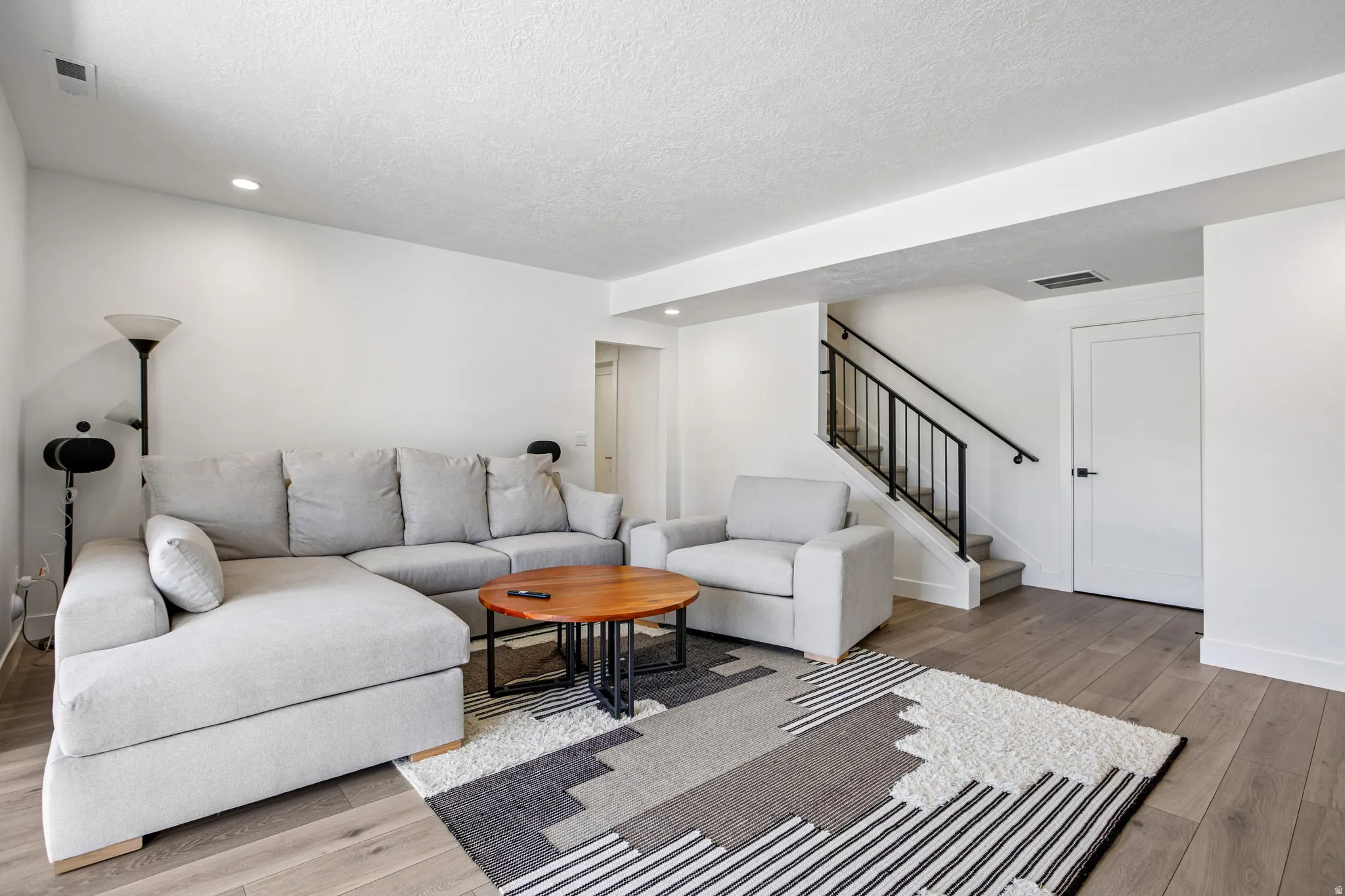 Open living area featuring wood-finish flooring, recessed lighting, and a contemporary staircase with black railings