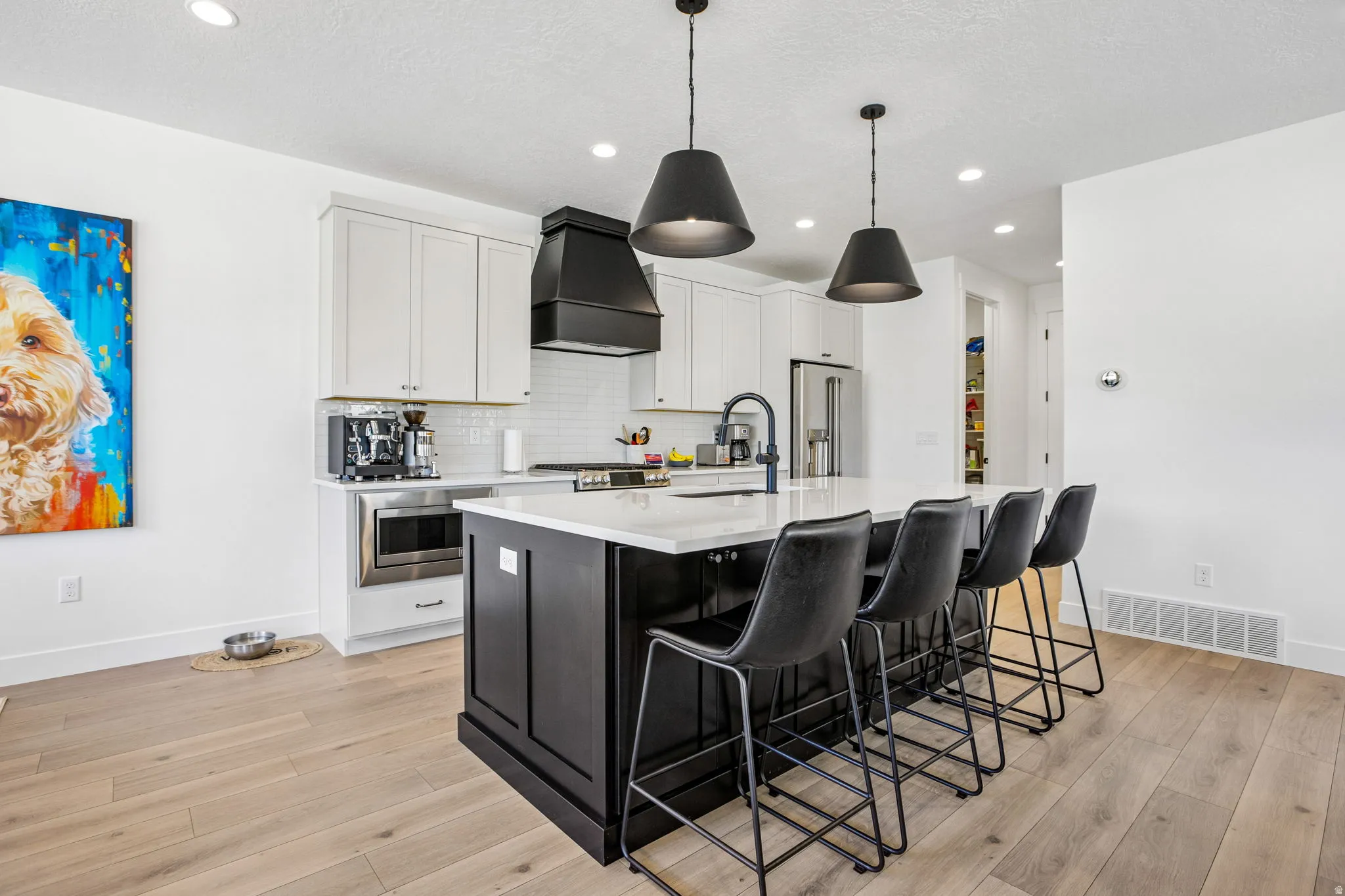 Modern kitchen featuring a large island with seating, pendant lighting, white upper cabinetry, a black range hood, and wood-finish flooring