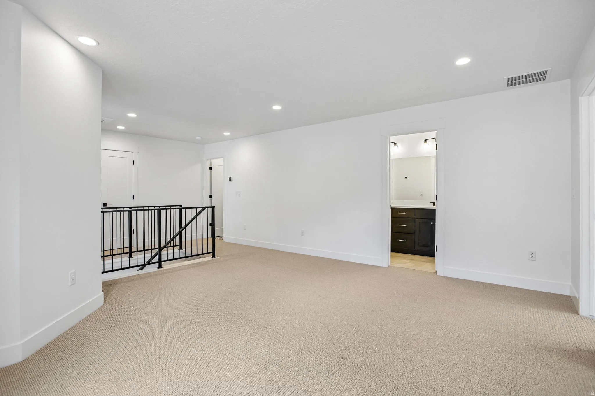 Spacious carpeted room featuring recessed lighting, white walls, and a black metal railing