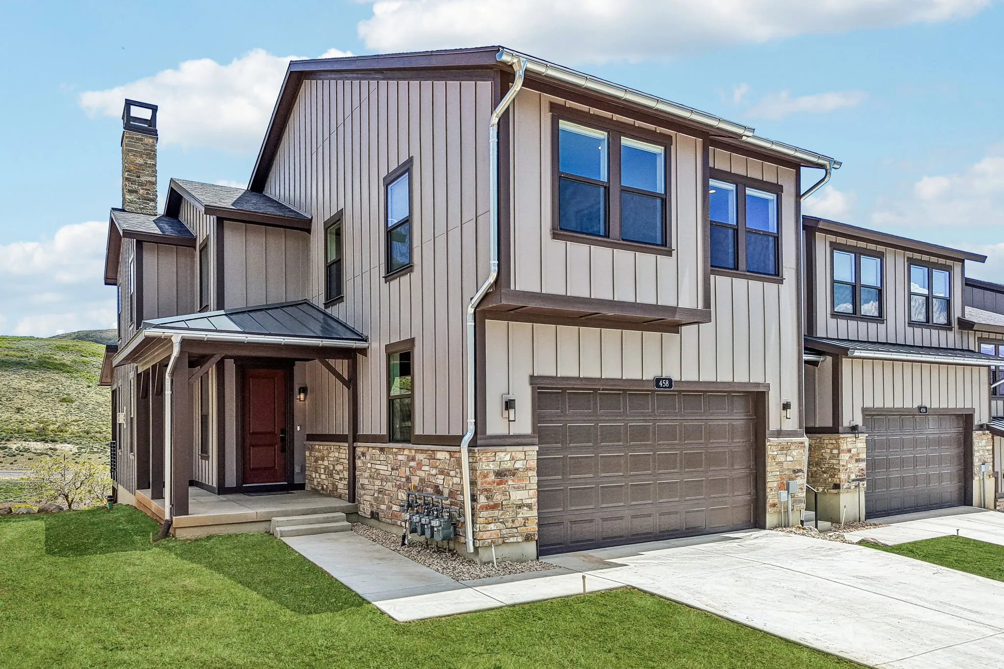 Modern exterior featuring vertical siding, stone accents, a covered front porch, an attached garage, and a prominent chimney