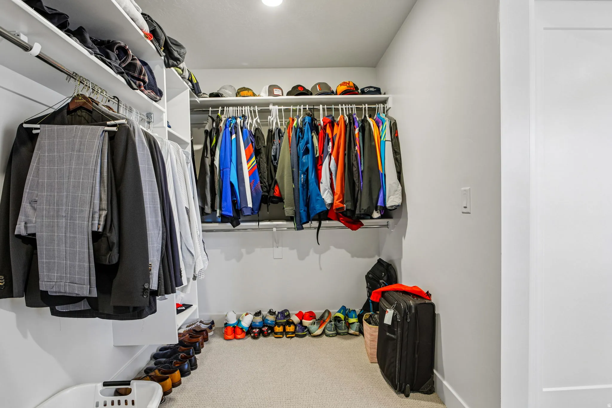 Spacious closet featuring white shelving, multiple hanging rods, and light-toned carpeting