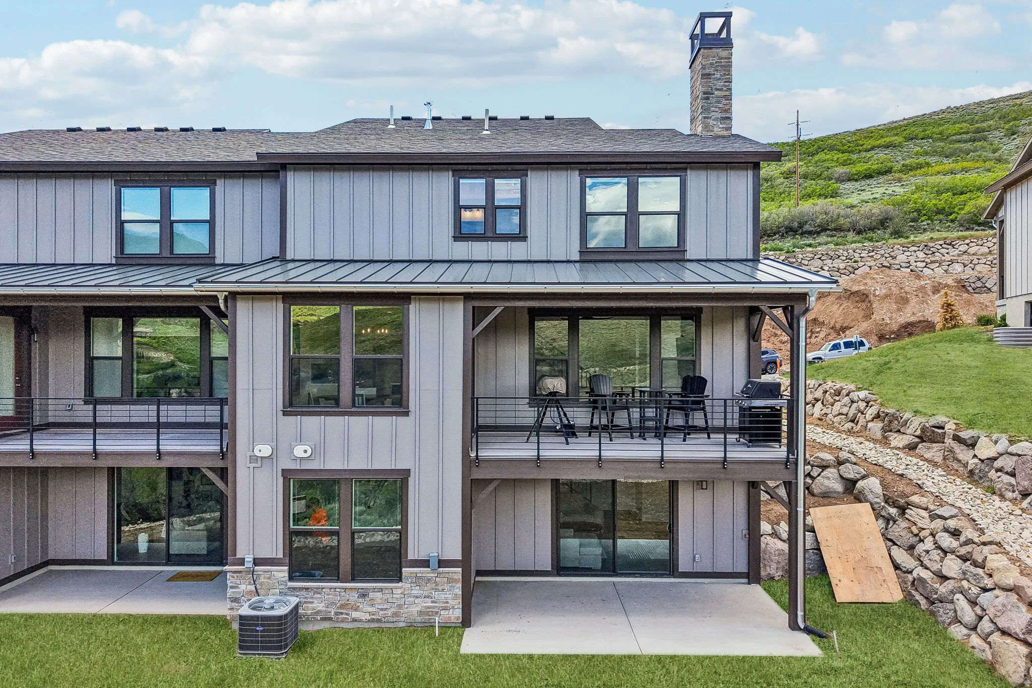 Modern townhome exterior featuring vertical siding, dark framed windows, a spacious upper-level balcony, and a ground-level patio