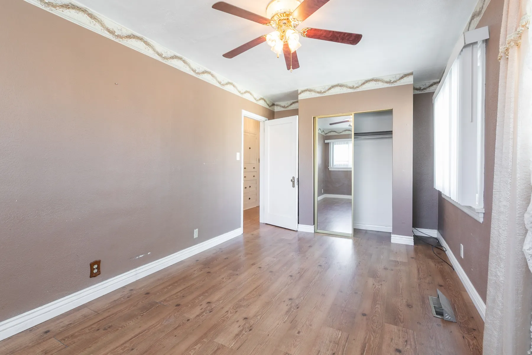 Interior room featuring wood-finish flooring, a ceiling fan with light fixture, white baseboards, and a window with blinds