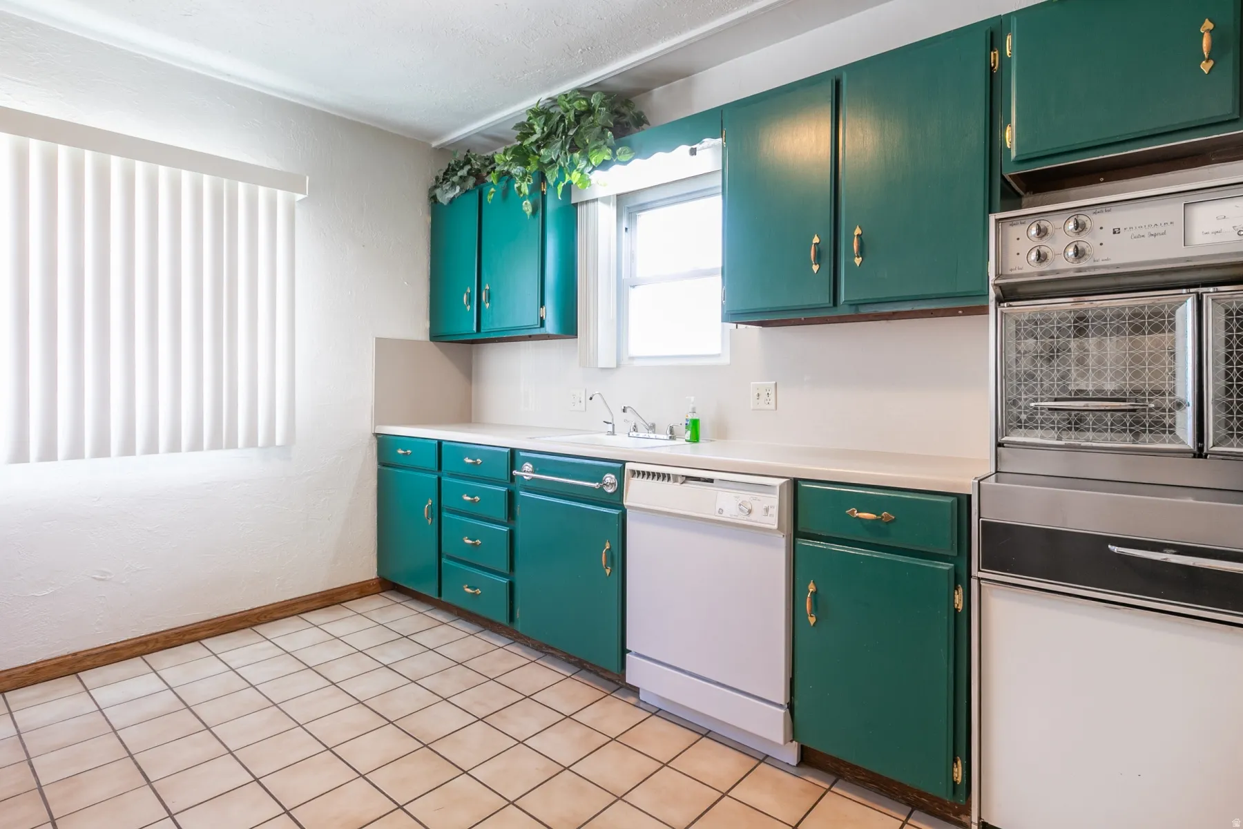 Kitchen featuring green cabinetry with gold-toned hardware, a white dishwasher, and a built-in double oven