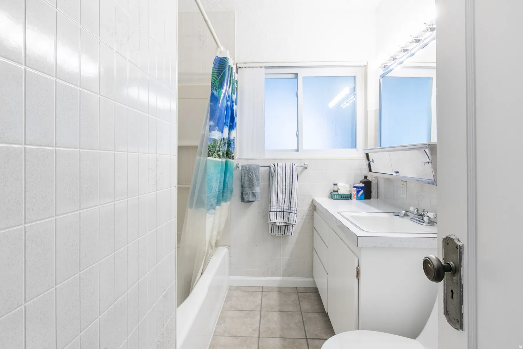 Bathroom featuring a white subway tile shower surround, a built-in bathtub, a window with frosted panes, a single vanity with storage, and a mirrored medicine cabinet