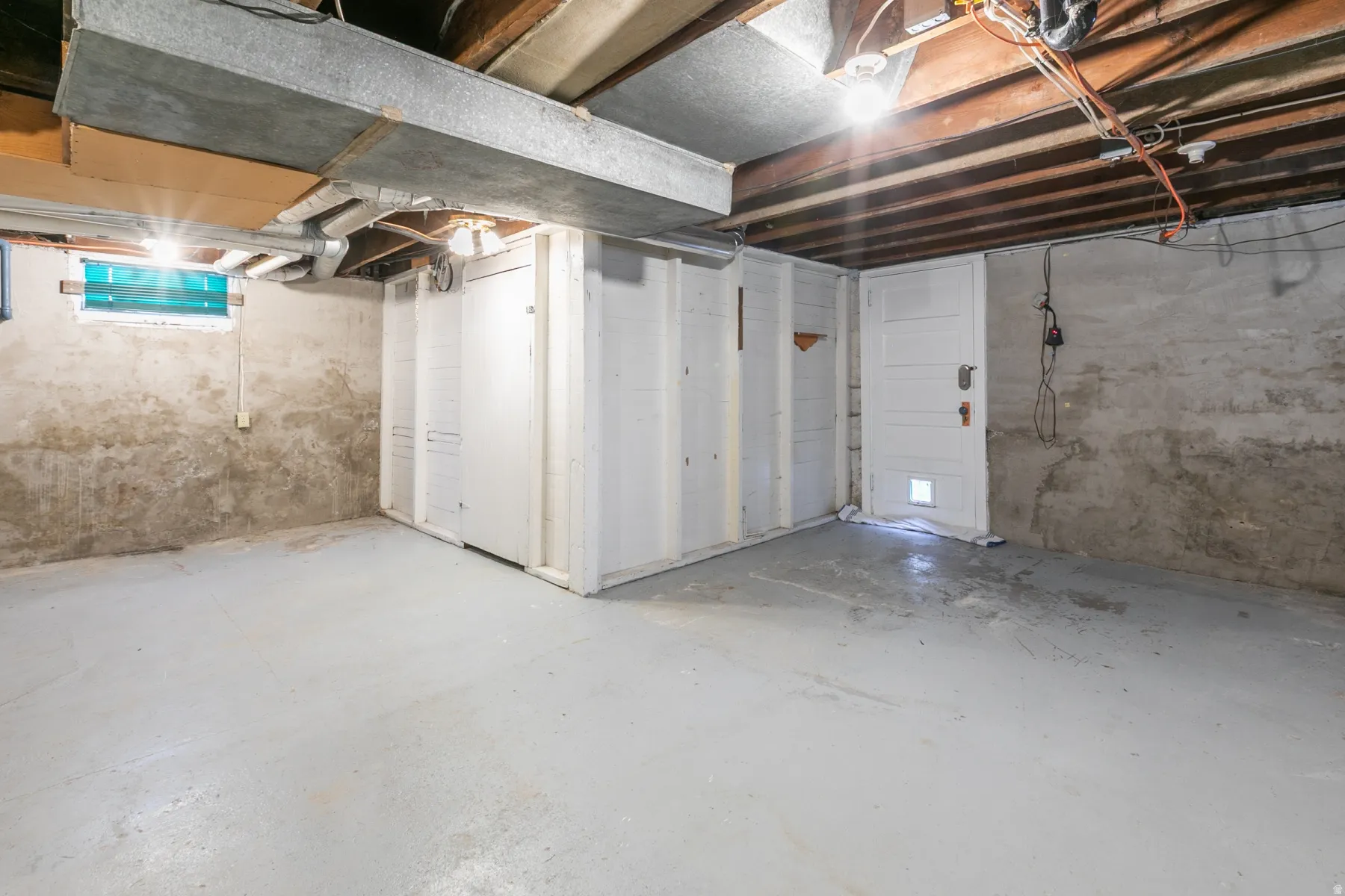 Unfinished basement space featuring exposed ceiling joists, painted concrete flooring, and a small window