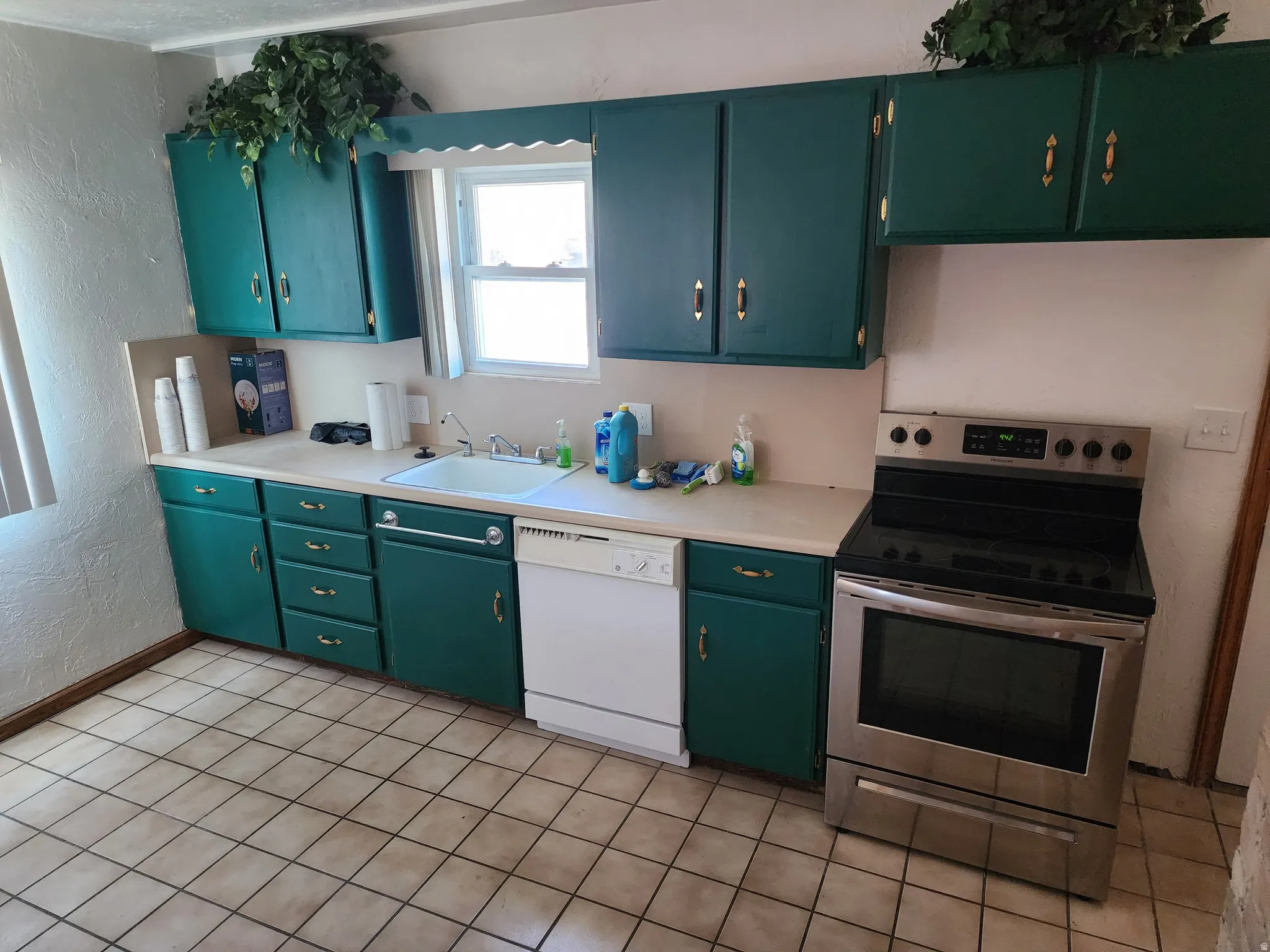 Kitchen featuring teal cabinetry with gold-tone hardware, a stainless steel range with a flat cooktop, a white dishwasher, and a white sink