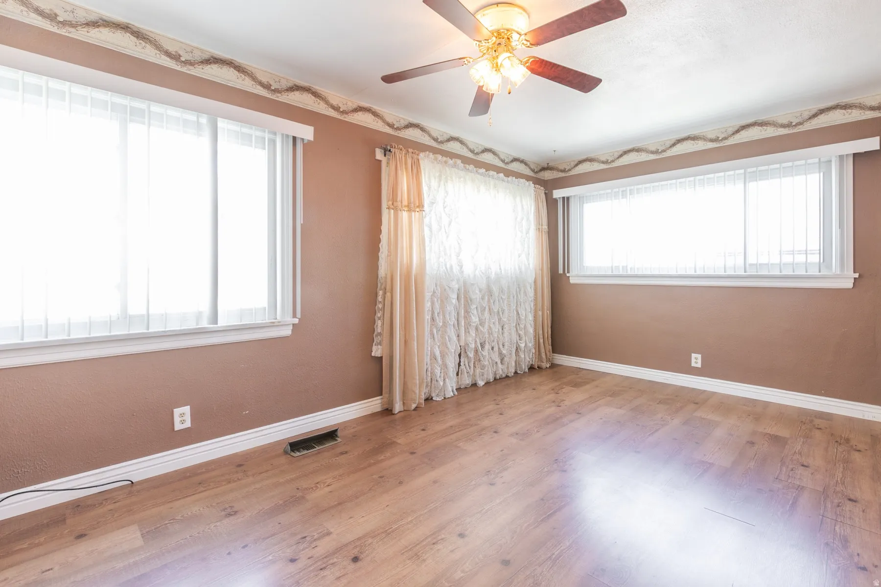Spacious interior room featuring wood-finish flooring, two large windows with white blinds, and a ceiling fan with integrated lighting