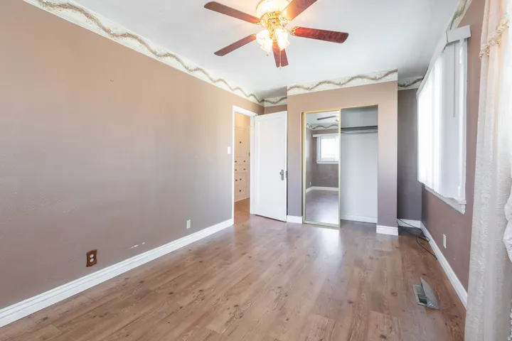 Interior room featuring wood-finish flooring, a ceiling fan with light fixture, white baseboards, and a window with blinds