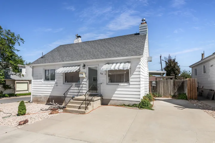 White siding exterior featuring a dark shingle roof, concrete driveway, and striped window awnings