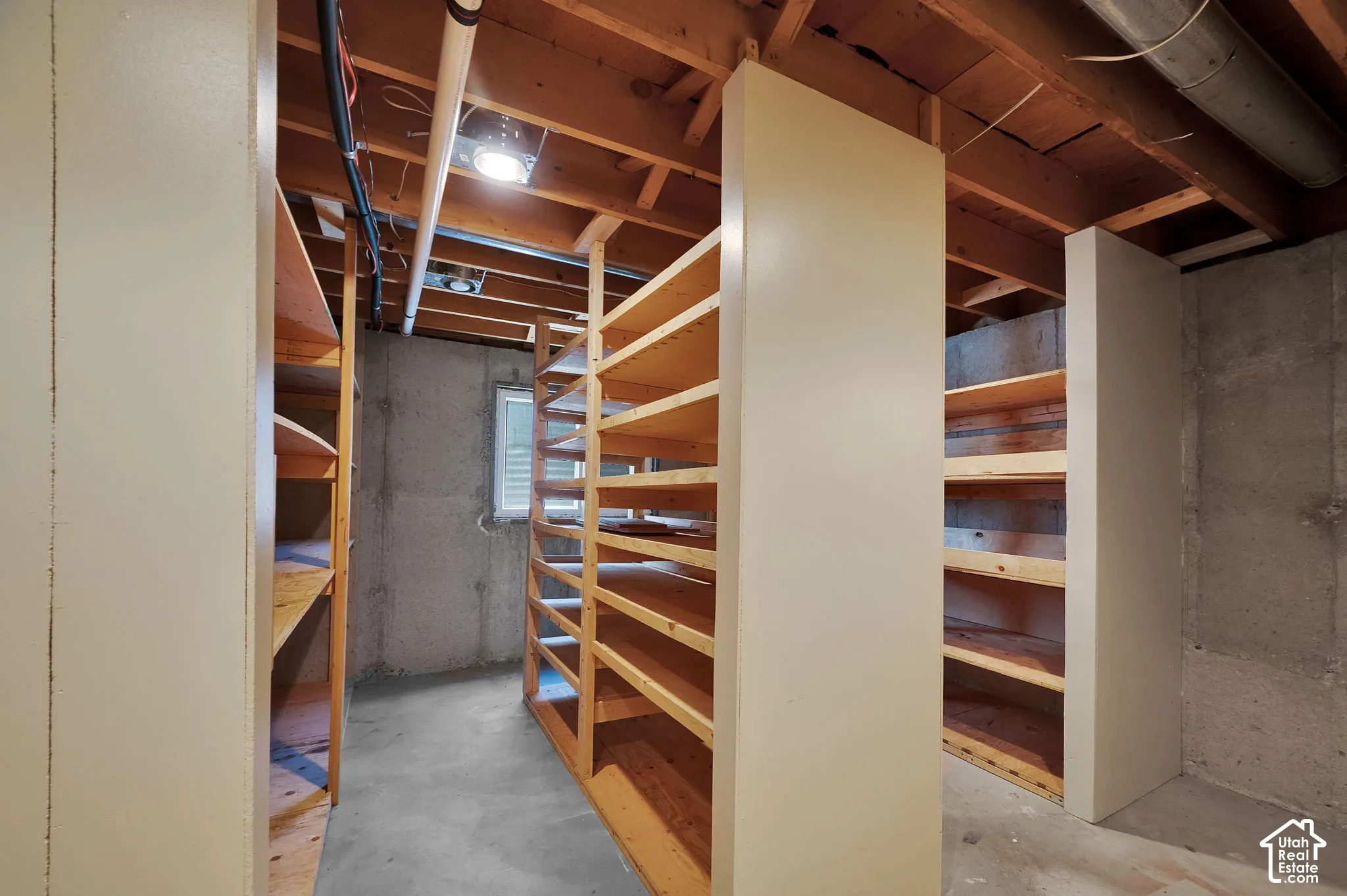 Spacious unfinished lower level featuring extensive built-in wooden shelving units, exposed ceiling joists, concrete walls, and concrete flooring