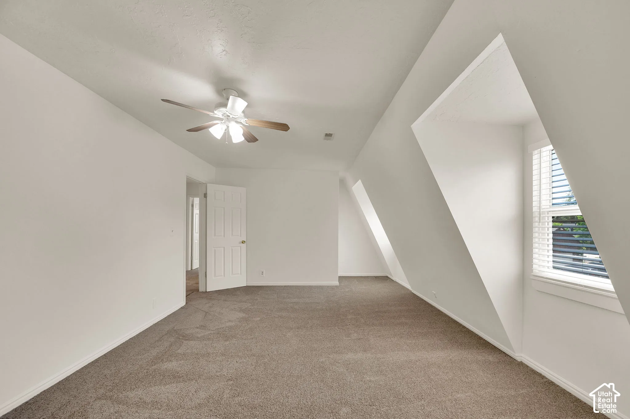 Spacious room featuring sloped ceilings, white walls, and neutral carpeting