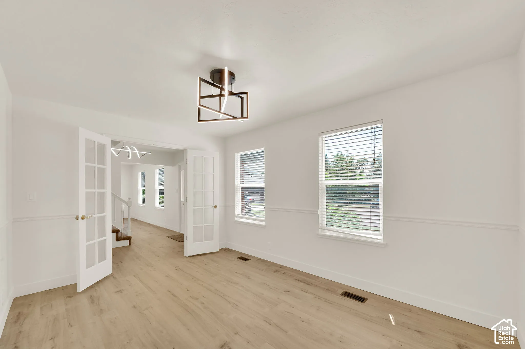 Room featuring light wood-finish flooring, white walls with wainscoting, and a modern geometric ceiling light fixture