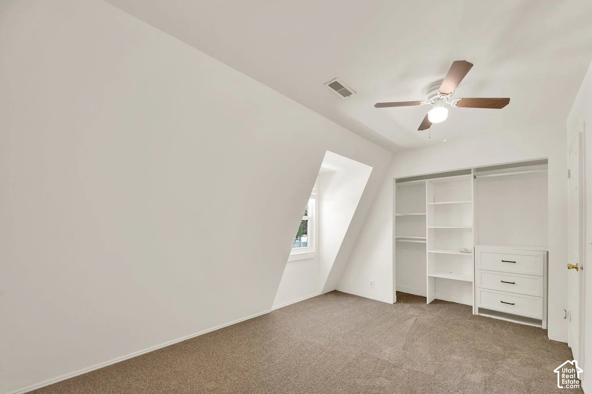 Attic room featuring a sloped ceiling, window, built-in shelving, built-in drawers with dark hardware, and a ceiling fan
