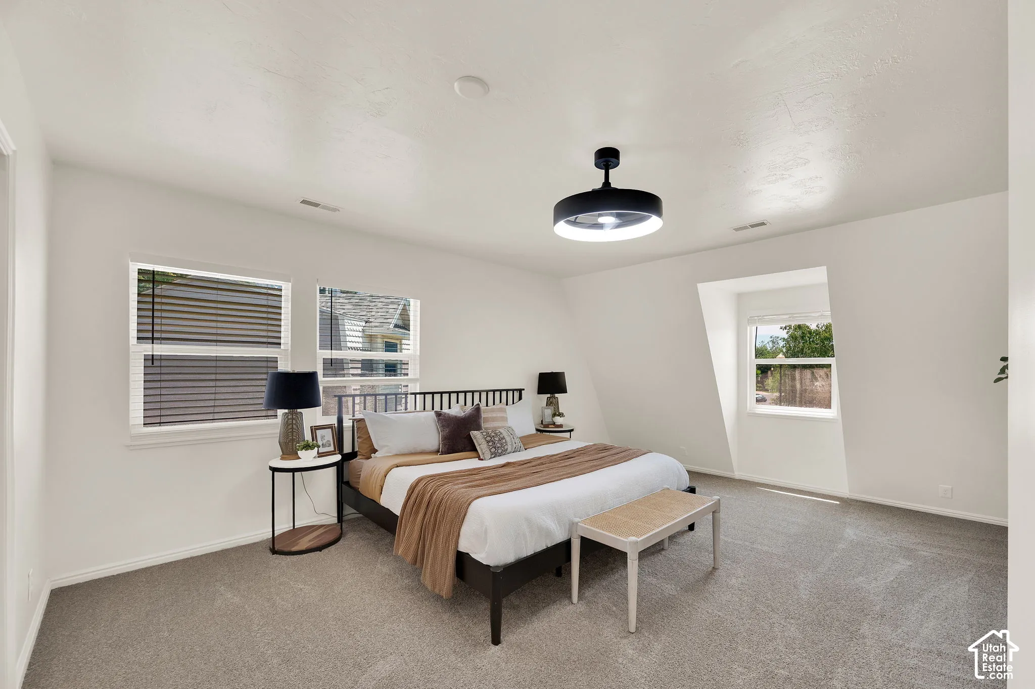 Spacious room with plush carpet flooring, multiple windows featuring blinds, and a contemporary ceiling light fixture